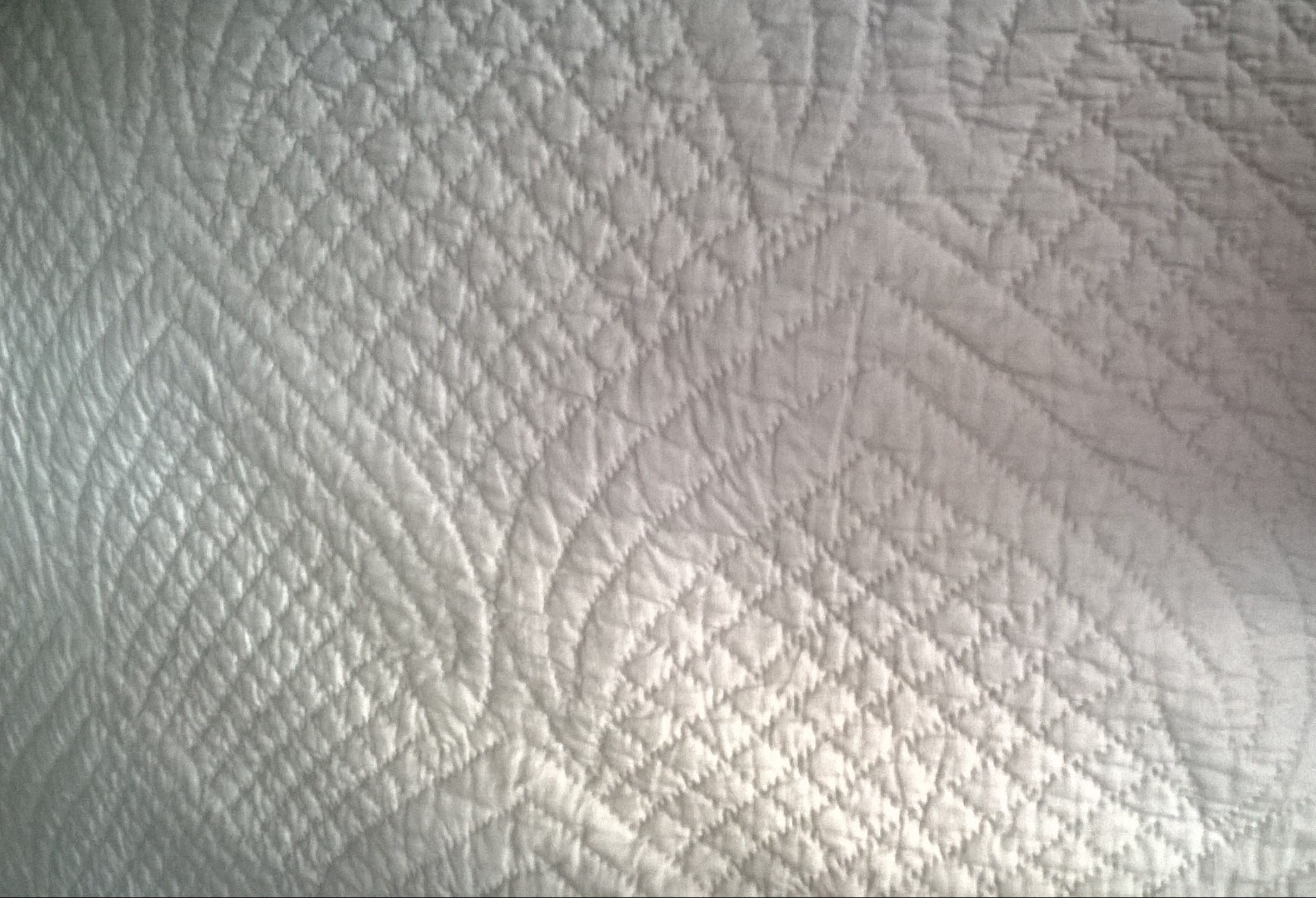 white quilting on a white background on a traditional North Country Quilt in which the stitches make the pattern.