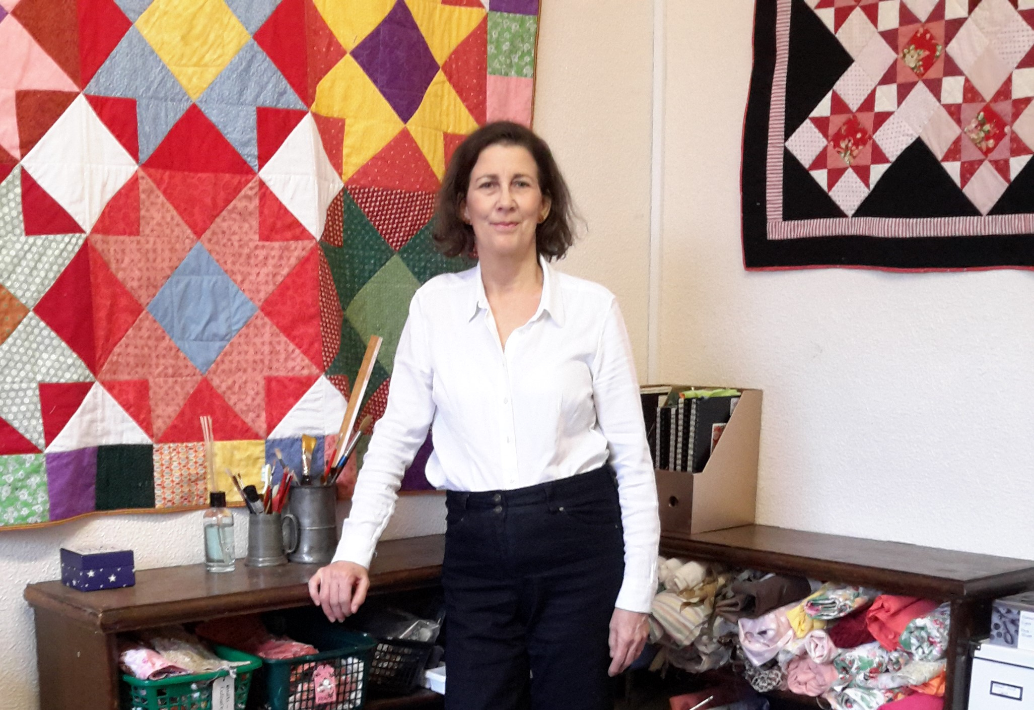 Amanda Jane Ogden in her studio with quilts on the wall: 'Colours of Mexico' (left) and 'Winter Roses' (right)
