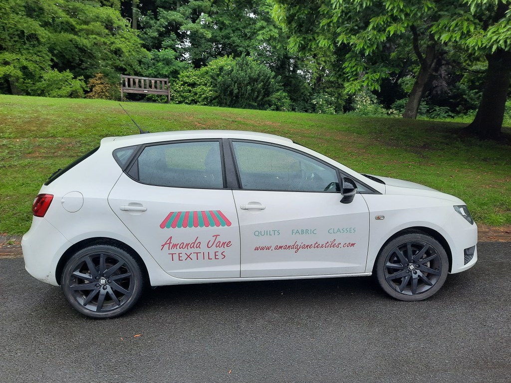 Amanda's car, a white Seat, complete with turquoise and pink decals advertising Amanda Jane Textiles