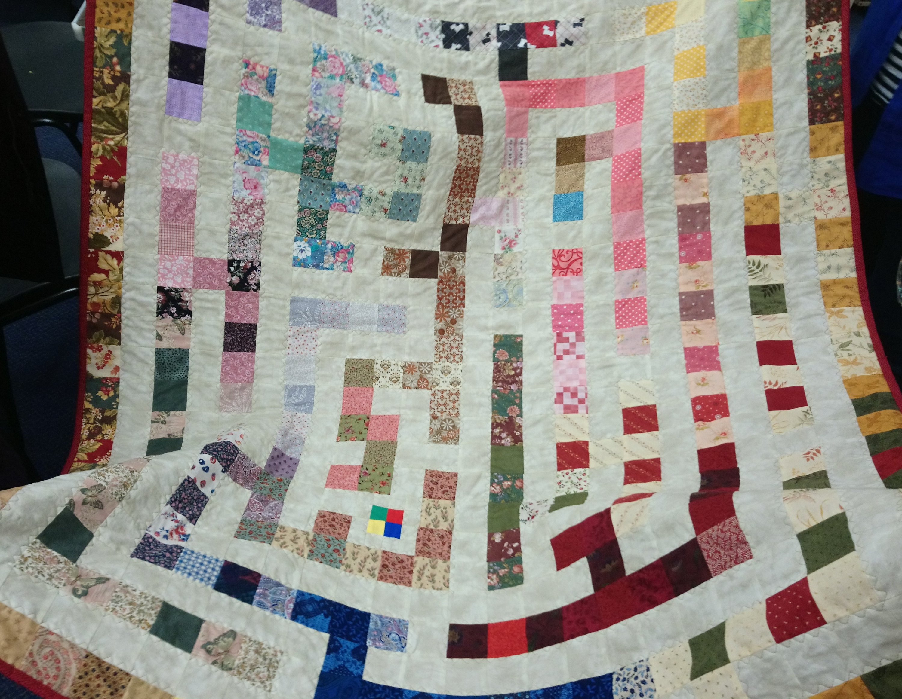 a quilt with a white background and multi-colured squares which form a maze