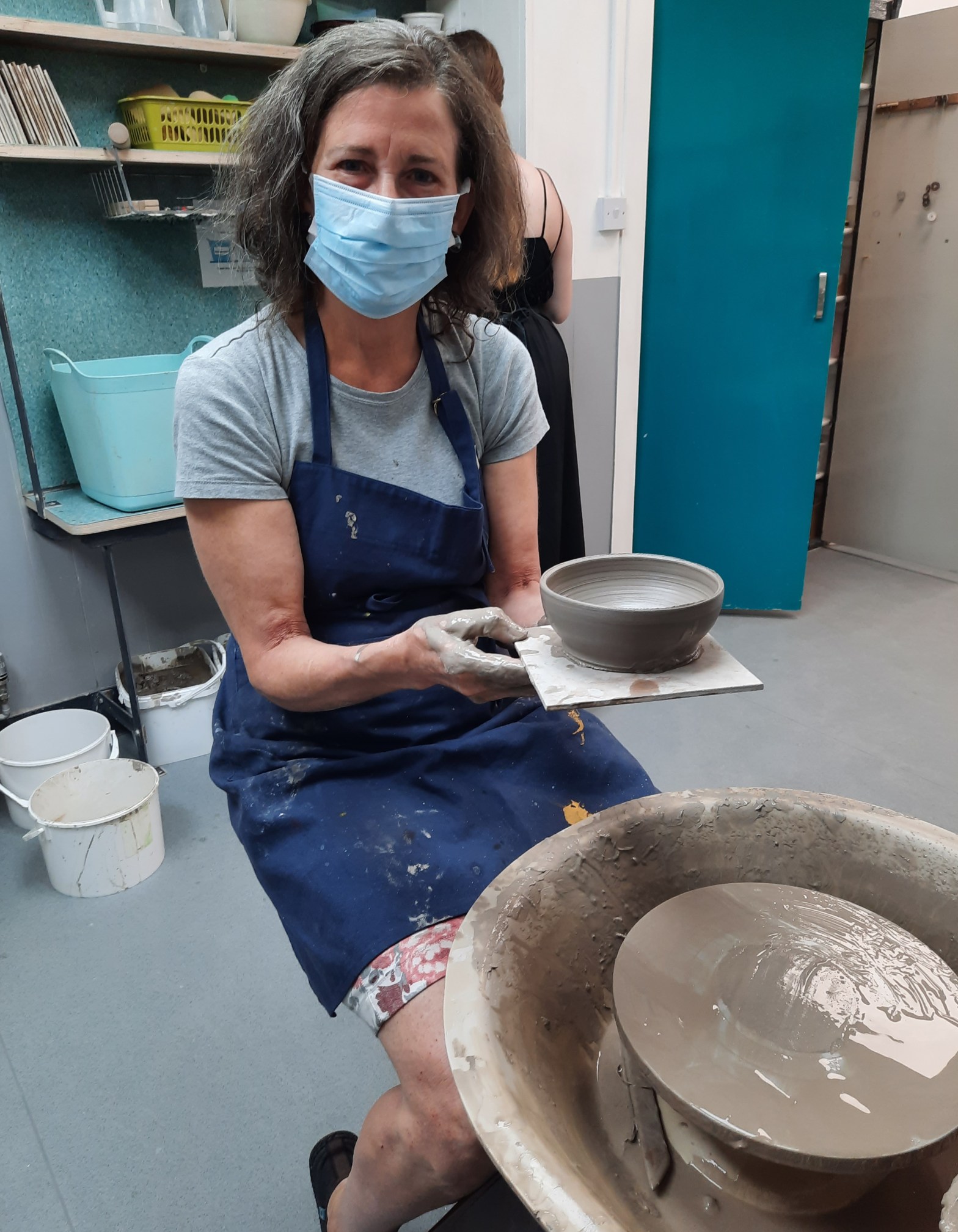 Amanda holding out a clay pot that she has just removed from the wheel