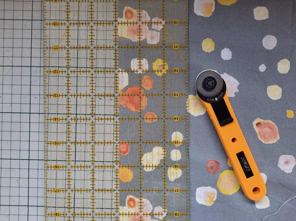 Cutting a two and seven-eighths inch strip from 'Micro-organisms' fabric by Amanda Jane Textiles, using a quilter's ruler and rotary cutter