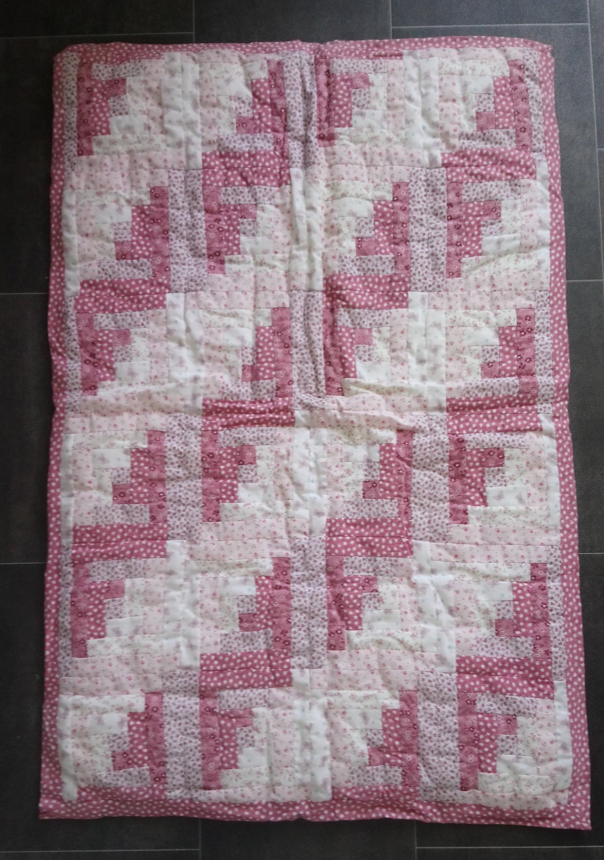 a cot quilt made using log cabin blocks in shades of pink