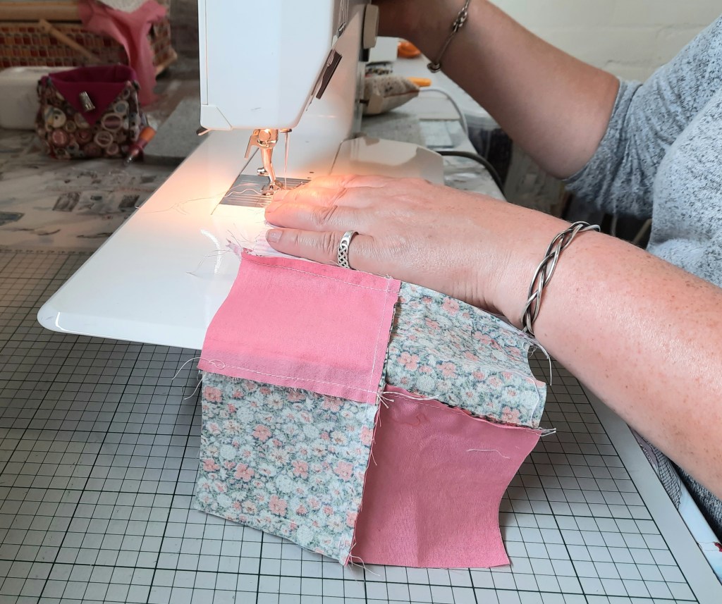 a person learning a new craft,  stitching a patchwork block in pink-coloured fabrics on the 'Quilt in a Day' course