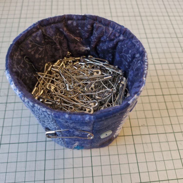 A textile canister filled with large, curved quilter's pins