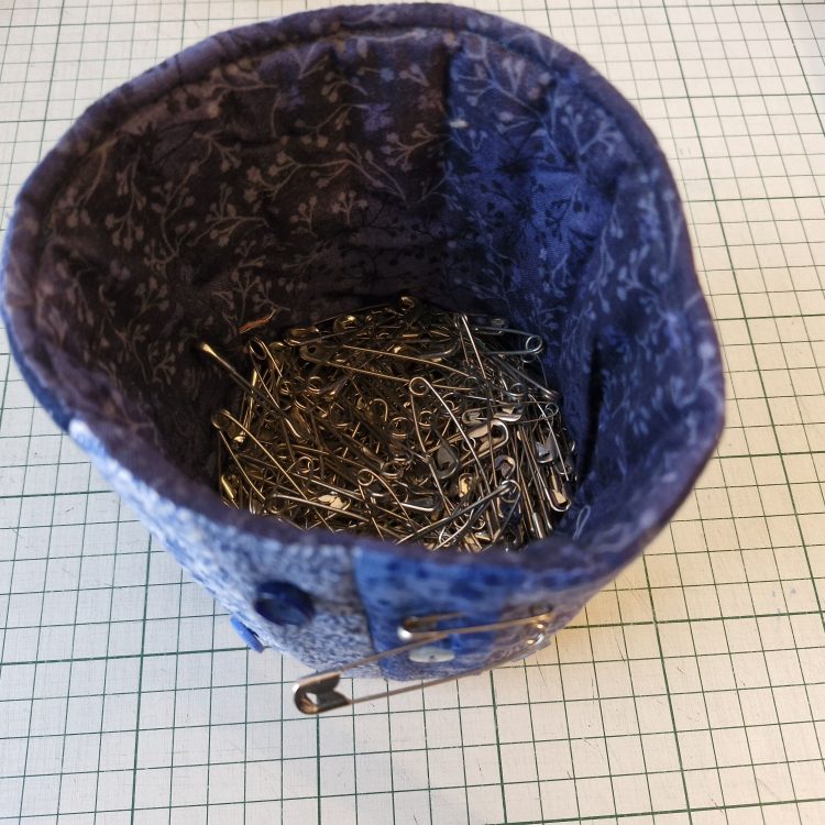 A fabric canister filled with straight safety pins