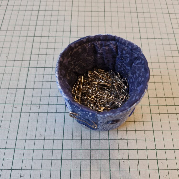 A textiles canister containing small, curved quilter's pins.